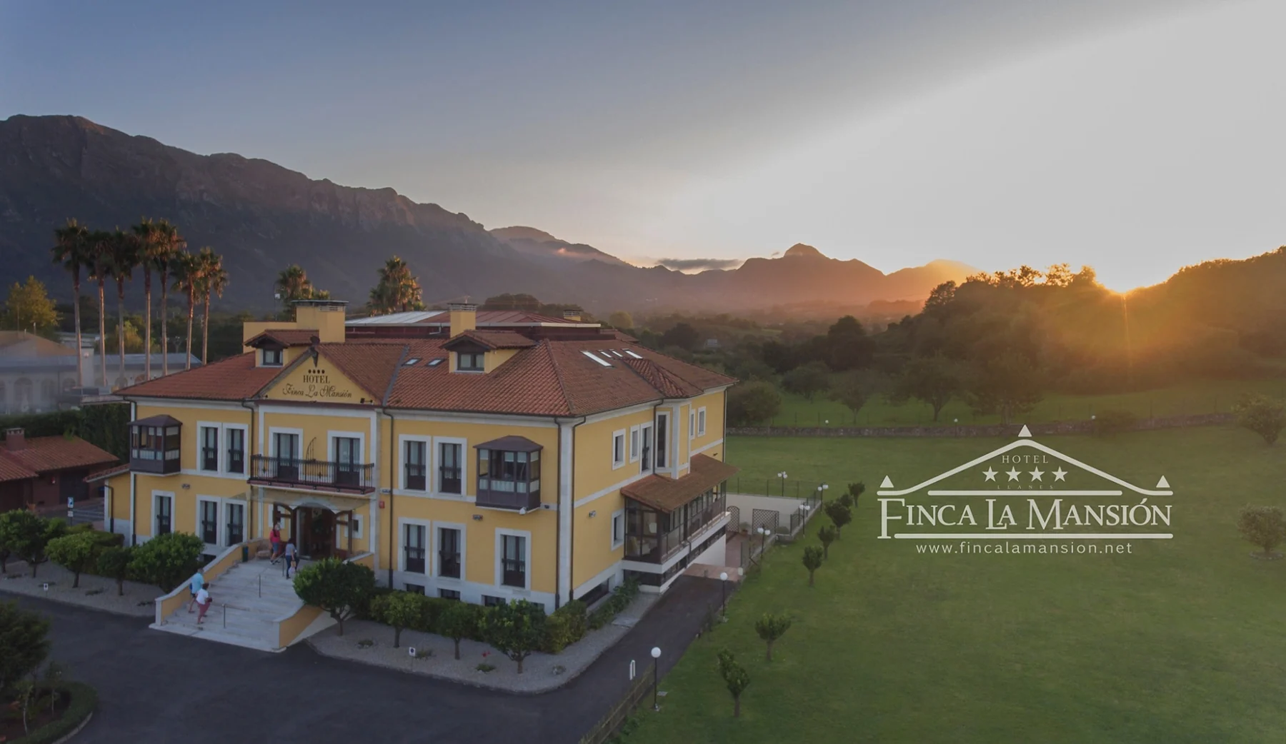 Hotel facade and gardens with the mountains at sunset
